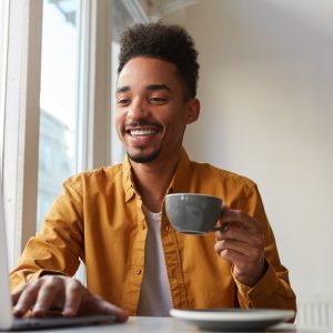 african american sitting table cafe working laptop wears yellow shirt drinks aromatic coffee communicates with his sister which is far another country enjoys work 2